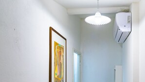 Ein schmaler Korridor mit Holzboden, weißen Wänden, einem Deckenventilator und einer Klimaanlage.