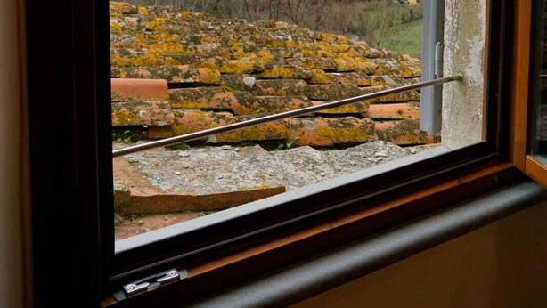 Ein Fenster mit Blick auf eine ländliche Landschaft, darunter Felder und ferne Berge.