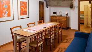 Ein Essbereich mit Holztisch und Stühlen, ein blaues Sofa sowie eine Küchenzeile mit Küchenschrank und Monitor.