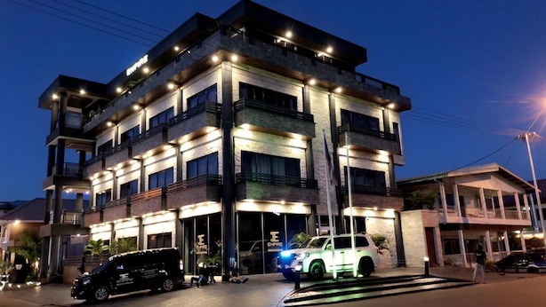 Un edificio de varios pisos con señalización iluminada, un coche estacionado en la entrada y una persona tirada en el suelo.