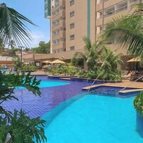 Piscina com bordas azulejadas, rodeada por palmeiras e cadeiras de descanso.