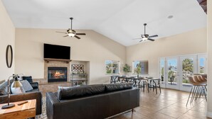 A spacious living room with a fireplace, a large black leather sofa, a dining area, and a ceiling fan. - Home in a boulder-filled neighborhood. 15 minutes to Joshua Tree National Park! (Yucca Valley)