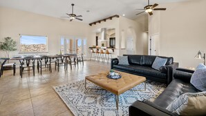 A spacious living room with a black leather sofa, a coffee table, and a dining area with a large window. - Home in a boulder-filled neighborhood. 15 minutes to Joshua Tree National Park! (Yucca Valley)