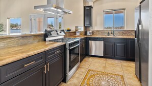 A modern kitchen with dark cabinetry, stainless steel appliances, and a granite countertop. - Home in a boulder-filled neighborhood. 15 minutes to Joshua Tree National Park! (Yucca Valley)
