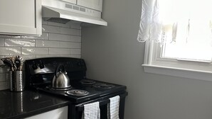 Cocina con armarios blancos, estufa negra y encimera negra. Se ve una ventana con cortina blanca.