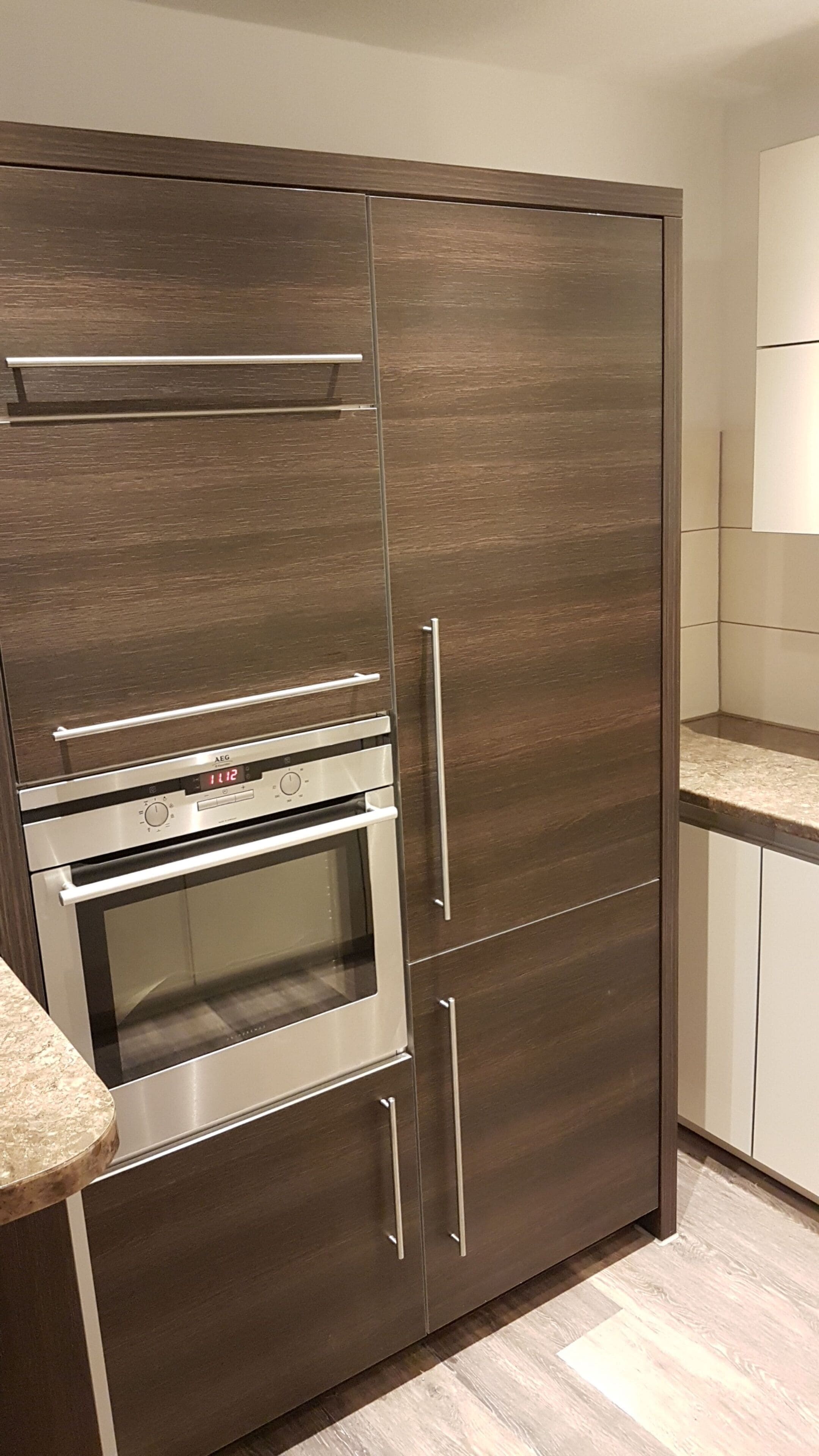 Una cocina moderna con horno empotrado y microondas, armarios de madera y encimera de granito.