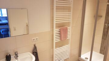 A bathroom with a white sink, a towel rack, and a glass shower enclosure.
