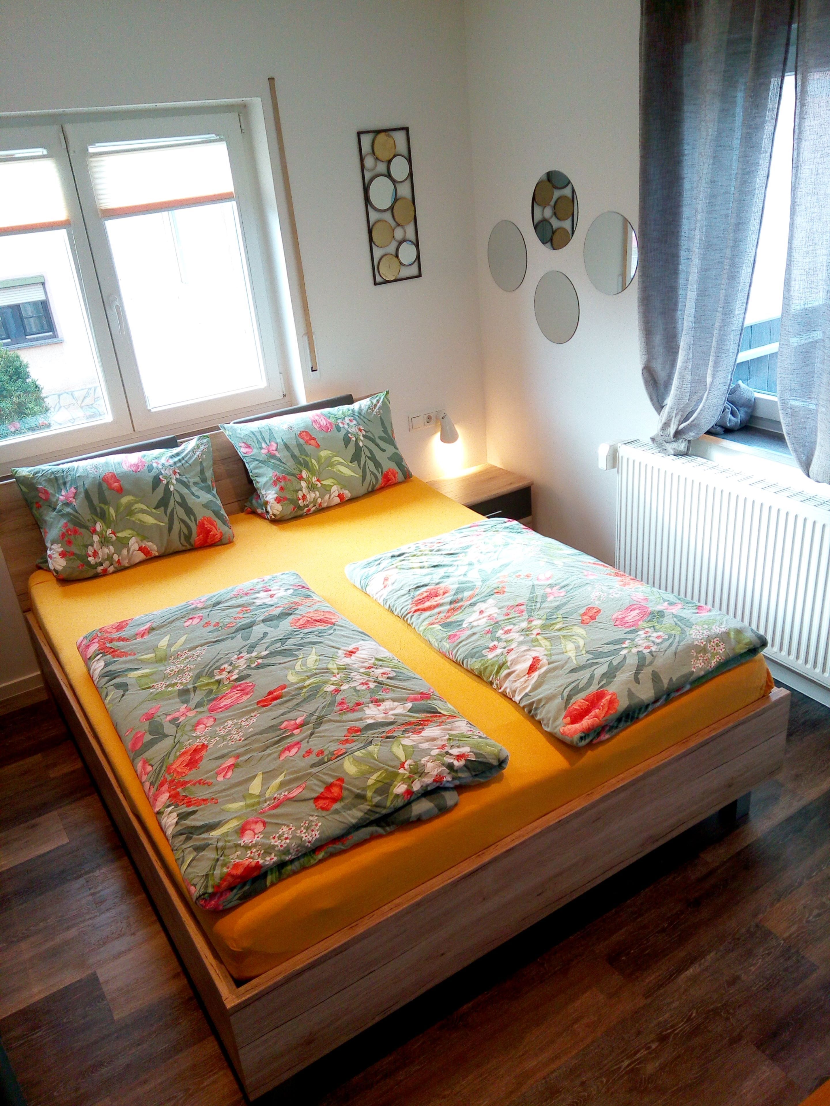 A bed with floral bedding, a bedside table with a lamp, and a window with curtains.
