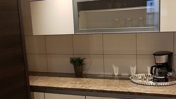 Eine moderne Küche mit weißen Schränken, einer Edelstahl-Dunstabzugshaube, einer Kaffeemaschine und einem Blumentopf auf der Arbeitsplatte.