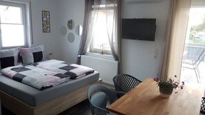A bedroom with a bed, a wooden table, a chair, a TV, and a window with curtains. - Ferienwohnung Busch (Rust)