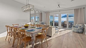 A spacious dining area with a wooden table and chairs, a chandelier, and a view of the ocean through large windows. - Beachfront, Pool, Amazing Views, and Sleeps 14 (Panama City Beach)