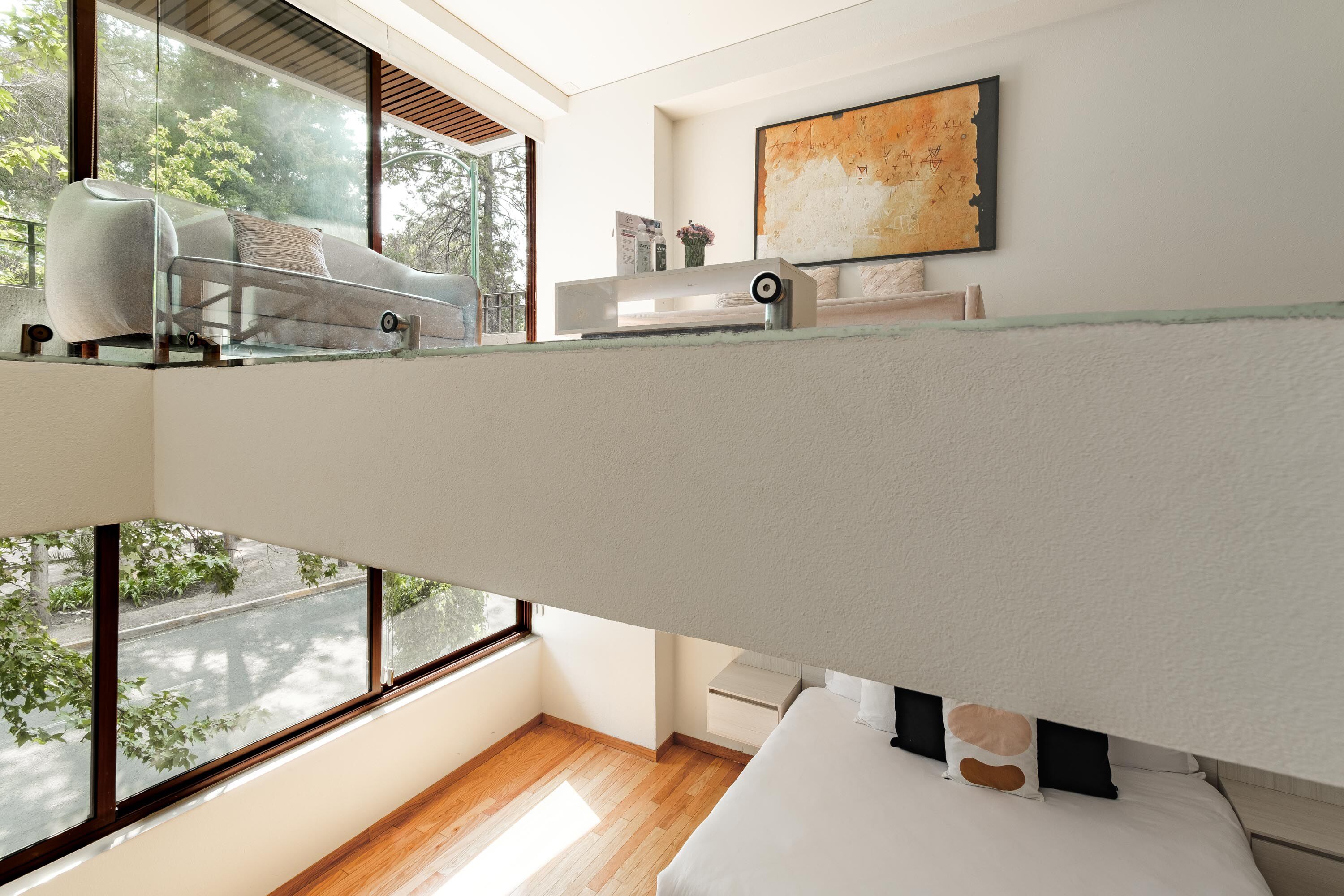 A modern bedroom with a bunk bed, a glass-walled window, a wooden floor, and a large abstract painting on the wall.