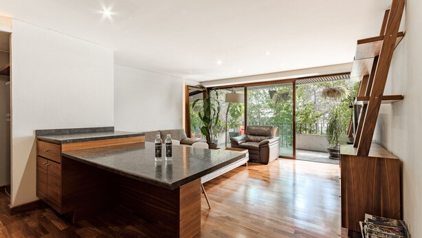Eine moderne Küche mit einer großen Kochinsel, Holzboden und Blick auf einen Balkon mit Pflanzen.