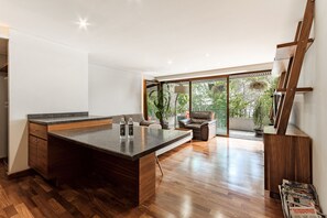 Una cucina moderna con un'isola grande, pavimento in legno e vista su un balcone con piante.