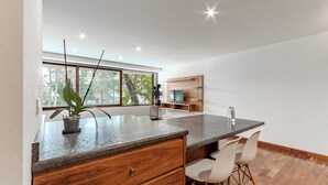 Eine moderne Küche mit Holztischplatte, weißen Stühlen und einem großen Fenster.