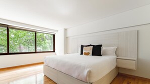 Ein modernes Schlafzimmer mit einem großen Bett, einem Fenster mit Blick auf Bäume und einem Holzboden.