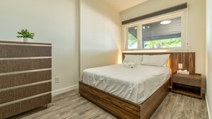 Une chambre à coucher avec un lit en bois, une table de chevet, une commode et une fenêtre avec des stores.