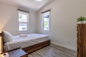 A bedroom with a bed, two windows, a wooden wardrobe, and a small table with a tissue box. - Cottage 4: Beachfront Cottage Escape (Wainfleet)