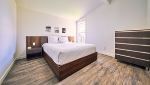 Quarto com cama de madeira, mesa de cabeceira, cômoda e janela com vista.