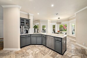 A spacious kitchen with a large island, dark gray cabinets, and a marble floor. - Beautiful Gated Home with Pool! (Austin)