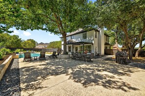 Eine überdachte Terrasse im Freien mit Pool, Sitzgelegenheiten und Grillbereich, umgeben von Bäumen.