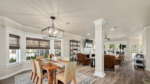 A spacious living area with a wooden dining table, wicker chairs, a fireplace, and a large window with blinds. - Beautiful Gated Home with Pool! (Austin)