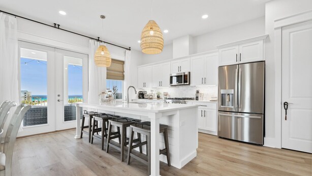 A modern kitchen with a large island, white cabinetry, stainless steel appliances, and a view to the outside. - Grand Retreat I! 4BR 5BA Sleeps 15! Private Pool! Luxury and Comfort Await! (Panama City Beach)