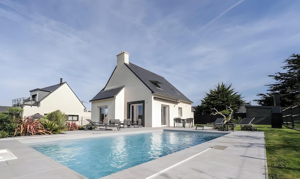 A residential property with a swimming pool, a patio with outdoor furniture, and a large tree.