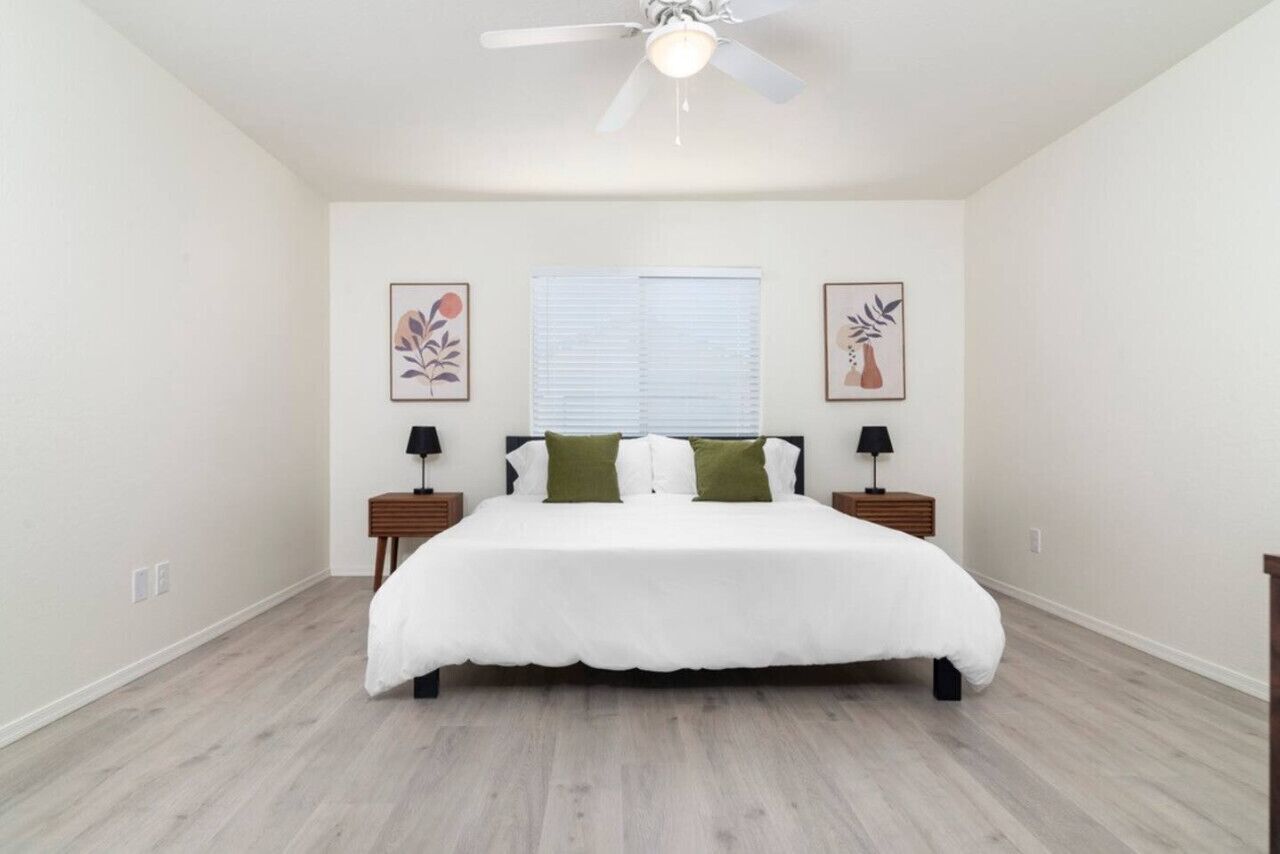A bedroom with a large bed, two nightstands, a ceiling fan, and two framed pictures on the walls.