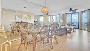 A spacious living area with a dining table, chairs, and a large window offering a view. - Award-Winning Resort Amenities | Shipwatch 321D (Isle of Palms)