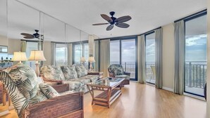 A spacious living room with wicker furniture, large windows, and a balcony. - Award-Winning Resort Amenities | Shipwatch 321D (Isle of Palms)