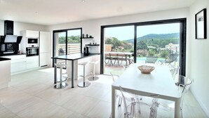 A modern kitchen with a dining area, large windows, and a view of a pool and greenery. - Villa Pietra Avec Piscine Privée à 300 Mètres de la Plage (Conca)