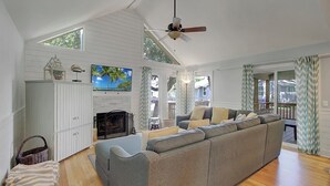 A spacious living room with a large gray sectional sofa, a fireplace, a ceiling fan, and a television. - Award-Winning Resort Amenities | Lake Village 10 (Isle of Palms)