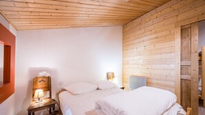 Ein Schlafzimmer mit Holzboden, einem Bett mit weißer Bettwäsche, einem Nachttisch mit Lampe und einem zusätzlichen Beistelltisch.
