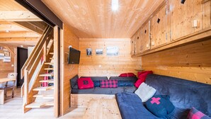 Ein Holzblockhaus-Interieur mit Treppe, einer Couch und einem Fernseher.