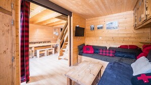 Ein Holzblockhaus-Innenraum mit einer Couch, einem Tisch, einem Fernseher und einer Treppe, die in einen anderen Raum führt.