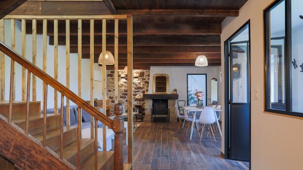 Una escalera de madera conduce a un comedor con paredes de piedra y una chimenea.