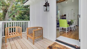 Een houten terras met twee rieten stoelen, een lantaarn en uitzicht op een kamer met een eettafel en stoelen.