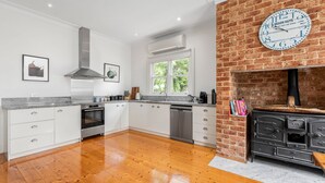Una cocina con armarios blancos, pared de ladrillo, un reloj grande y una chimenea.