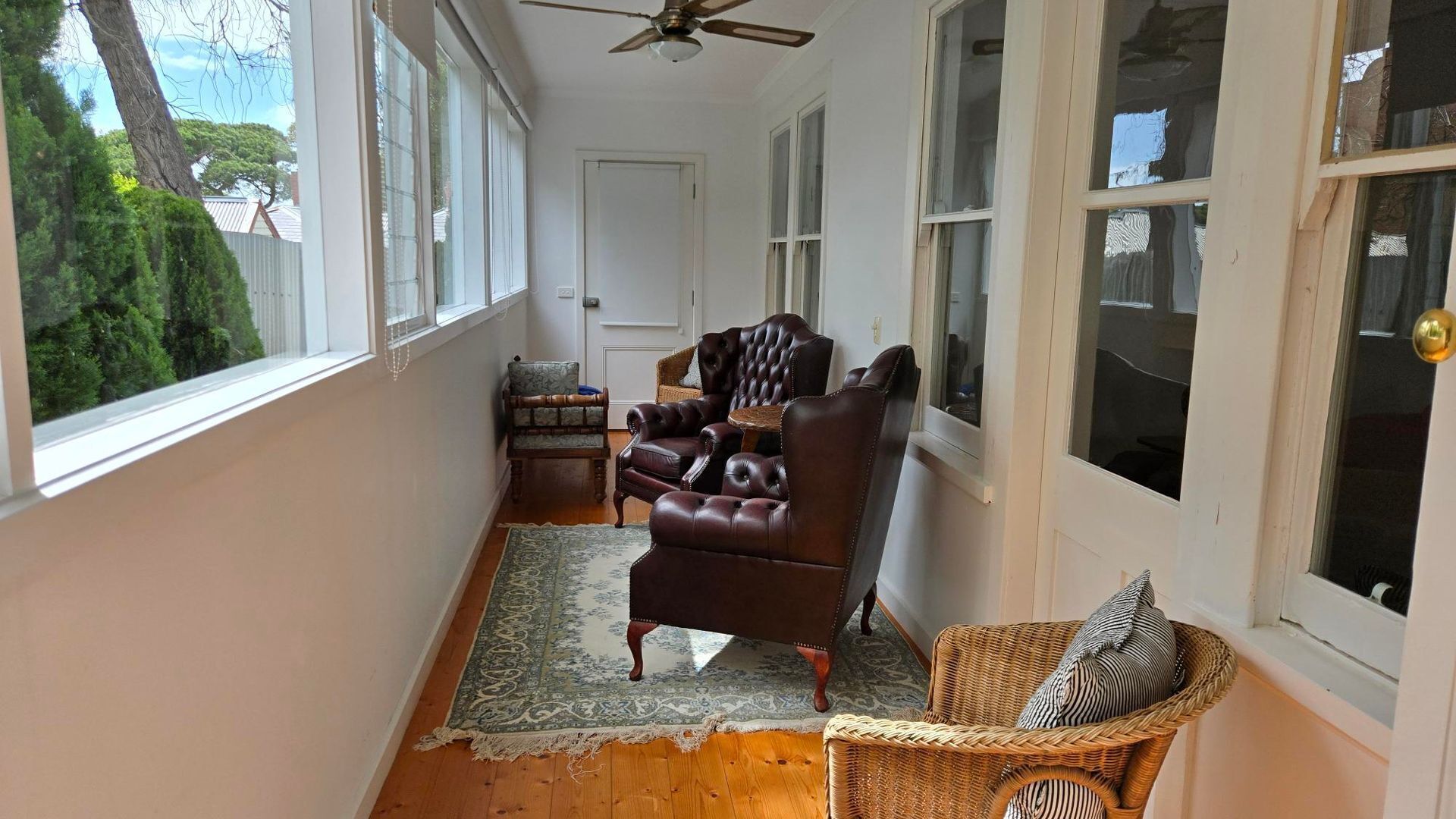 A sunlit room with a large window, a ceiling fan, and a wooden floor.