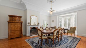 Un comedor con mesa de madera, sillas, candelabro, chimenea y un ventanal con persianas.