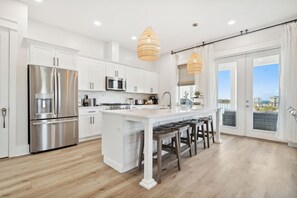 Cocina moderna con armarios blancos, electrodomésticos de acero inoxidable y una isla central con taburetes de bar.