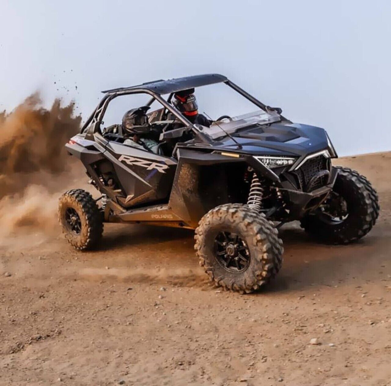 Un vehicle Polaris RZR tot terreny en moviment, aixecant pols.