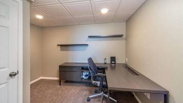 A room with a dark wooden desk, a black office chair, a telephone, and a shelf on the wall.