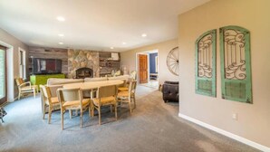 A spacious living area with a large dining table, comfortable seating, a fireplace, and a kitchen area in the background.