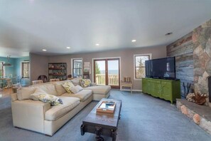 A spacious living room with a sectional sofa, a coffee table, a television on a green cabinet, and a stone fireplace.