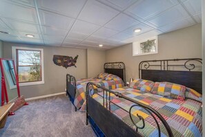 A bedroom with two metal-framed beds, a carpeted floor, a window with a view, and a wall map.