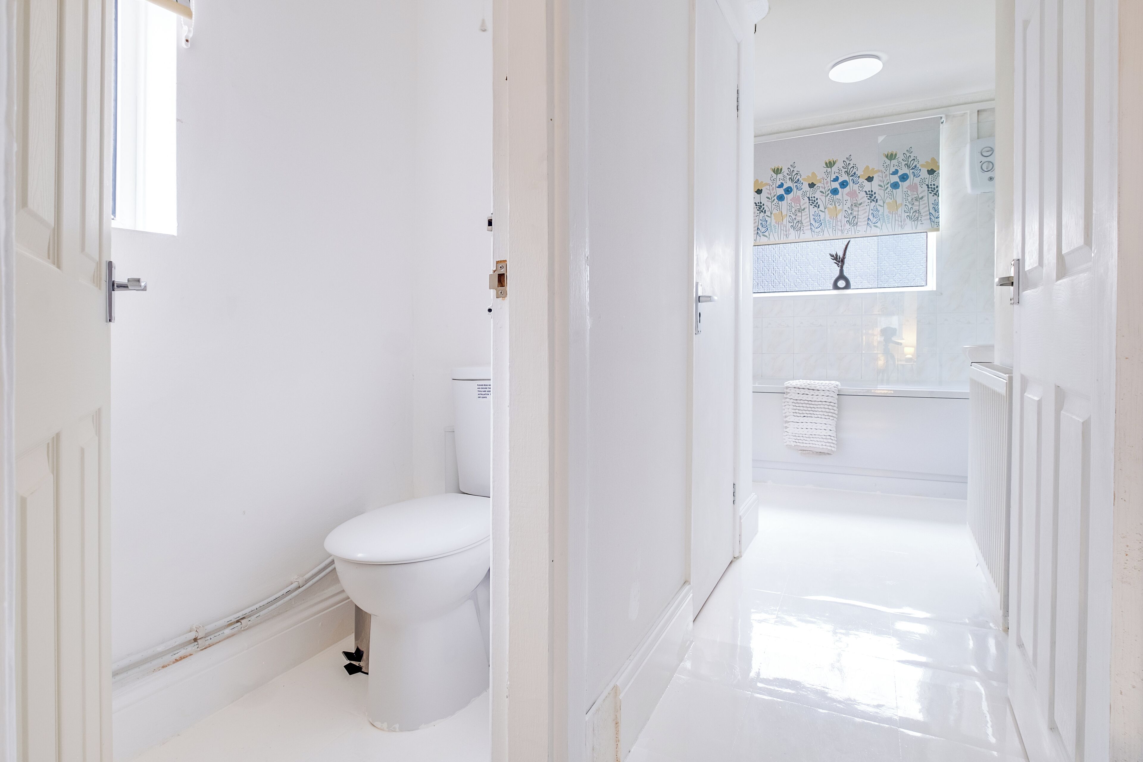 A white bathroom with a toilet, a shower, and a tiled wall with a floral pattern.