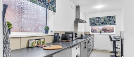 A modern kitchen with a washing machine, a toaster, and a window with a view of a beach.