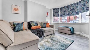 Una sala de estar con un sofá modular, un sofá pequeño, un tapete estampado y un ventanal con vistas a edificios.